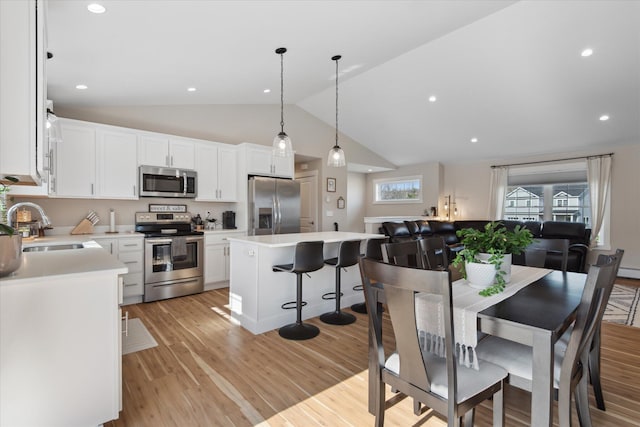 kitchen with a kitchen island, appliances with stainless steel finishes, vaulted ceiling, a sink, and light countertops