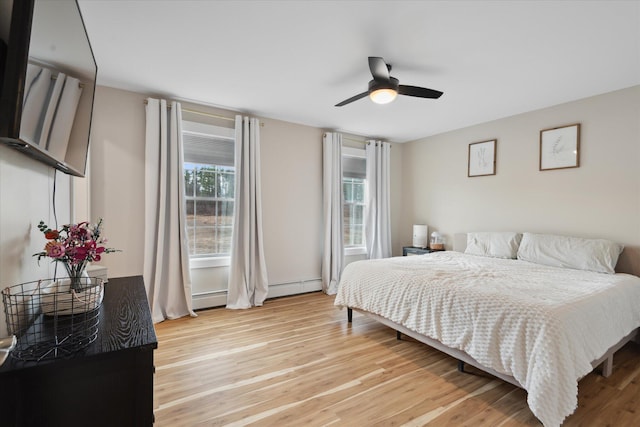 bedroom featuring ceiling fan, baseboard heating, a baseboard heating unit, and light wood-style flooring