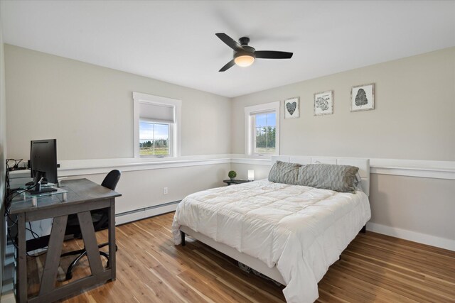 bedroom with a ceiling fan, a baseboard heating unit, and wood finished floors