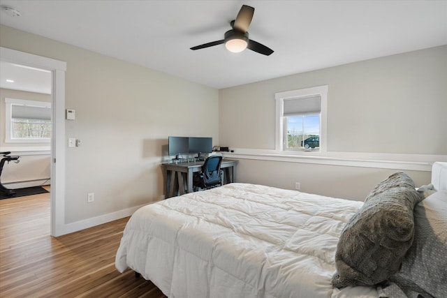 bedroom with baseboards, multiple windows, a baseboard heating unit, and wood finished floors