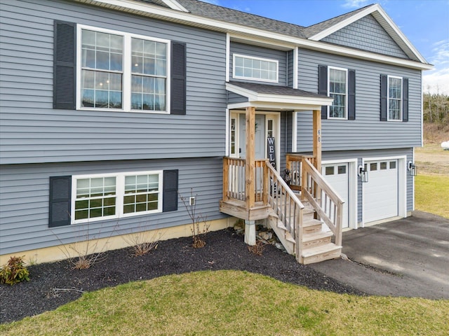 raised ranch featuring an attached garage, a front lawn, roof with shingles, and driveway