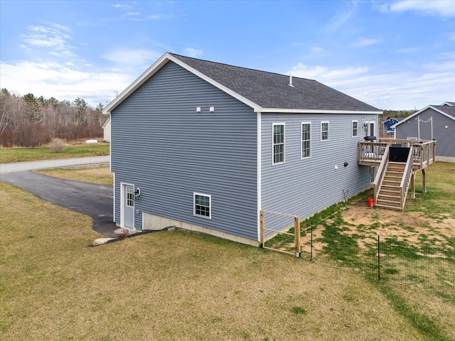 view of side of property featuring roof with shingles, a wooden deck, a yard, and stairway