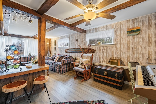 living area with beamed ceiling, a ceiling fan, wooden walls, and wood finished floors