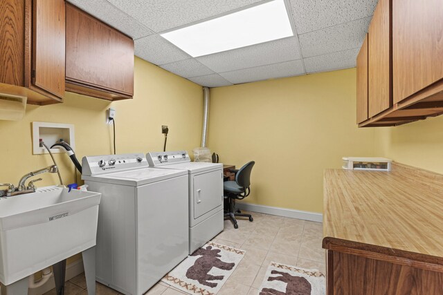laundry area featuring cabinet space, washer and dryer, a sink, baseboards, and light tile patterned floors