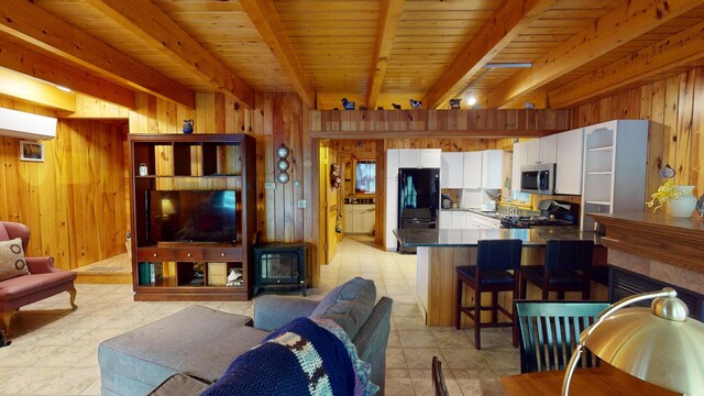 86 Webb Cove Dr, Lowell, ME 04493 - living room with wooden walls, a wood stove, light tile patterned flooring, and beam ceiling