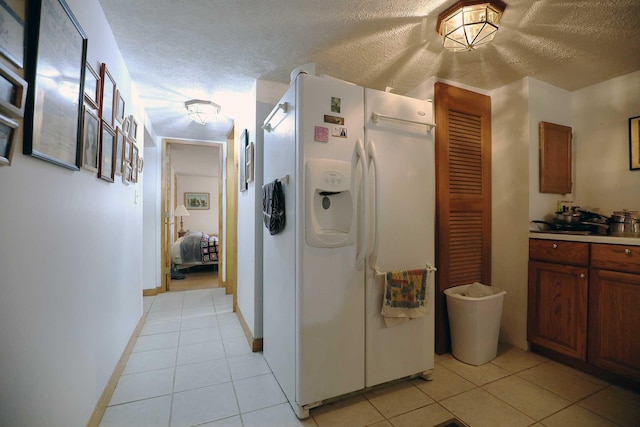 kitchen with brown cabinetry, light tile patterned floors, a textured ceiling, and white refrigerator with ice dispenser