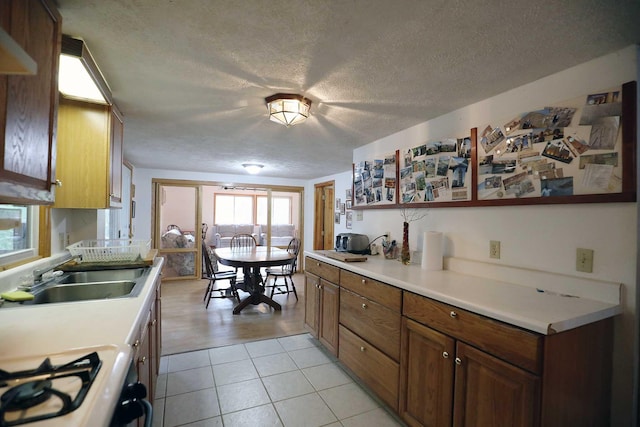 kitchen featuring a textured ceiling, a sink, gas range oven, light countertops, and brown cabinetry