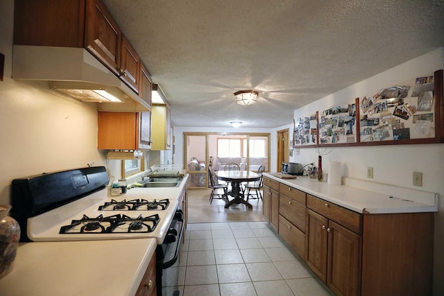 kitchen with a textured ceiling, brown cabinets, gas range oven, and a sink