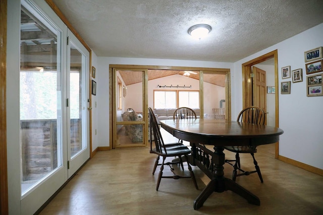 dining room featuring baseboards, light wood-style flooring, a textured ceiling, and lofted ceiling