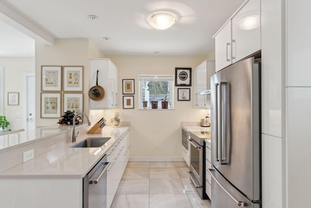 kitchen with a sink, baseboards, a peninsula, stainless steel appliances, and white cabinetry