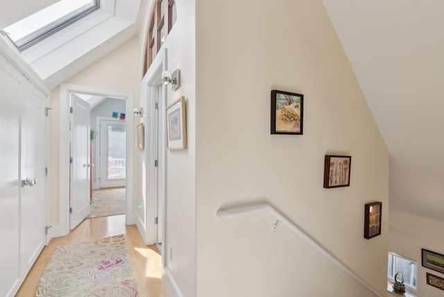 hall with baseboards, light wood-style flooring, and lofted ceiling with skylight