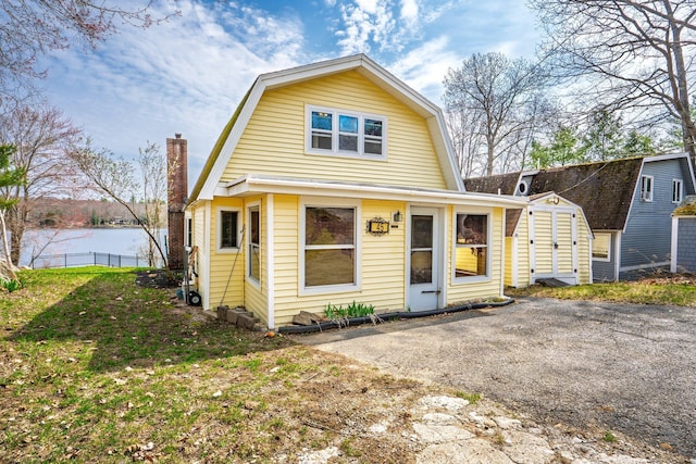 dutch colonial featuring a chimney, a gambrel roof, fence, and a shed