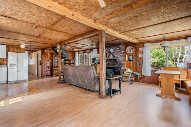 living area with a fireplace, wooden walls, stairway, light wood-type flooring, and a ceiling fan