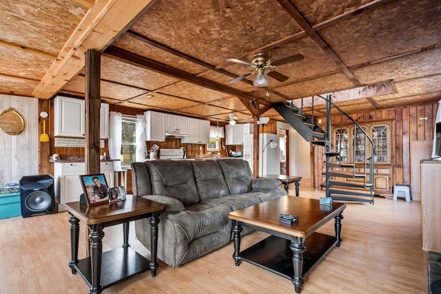 living area featuring stairway, ceiling fan, light wood-type flooring, and wood walls