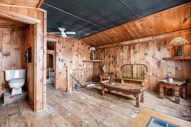 unfurnished room with a ceiling fan, vaulted ceiling, wood-type flooring, an upstairs landing, and wooden walls