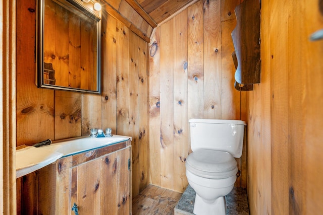 half bathroom with toilet, wood walls, a sink, and wood finished floors