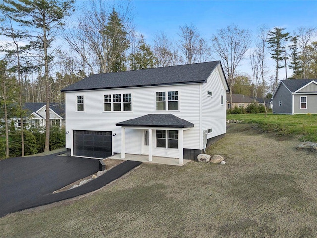 traditional-style house with an attached garage, asphalt driveway, a shingled roof, and a front lawn