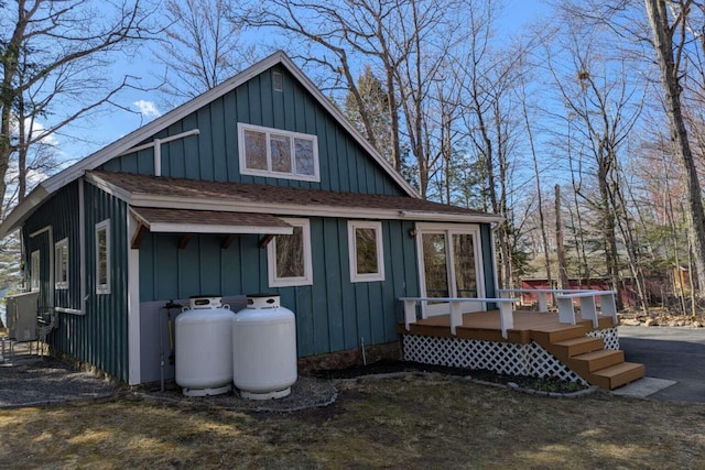 back of house with board and batten siding, a wooden deck, and a shingled roof
