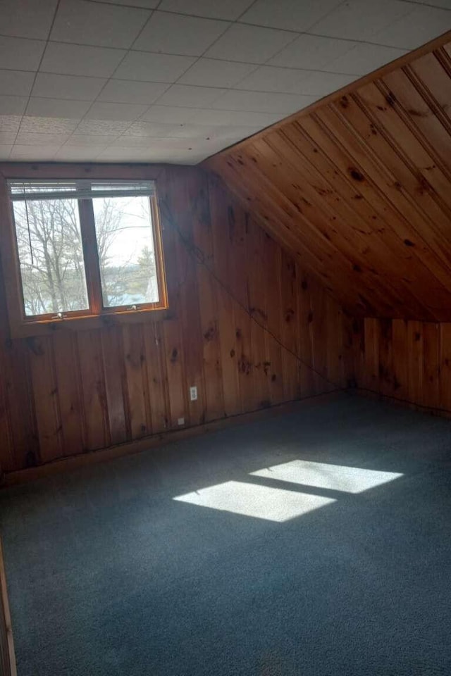 additional living space featuring wood walls, lofted ceiling, and carpet