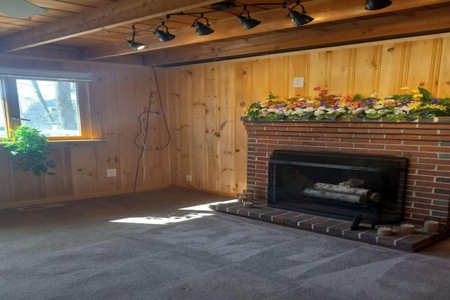 unfurnished living room featuring wood walls, carpet, a brick fireplace, and beam ceiling