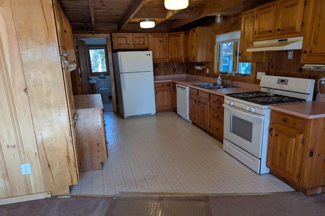 kitchen with a sink, beamed ceiling, white appliances, brown cabinetry, and under cabinet range hood