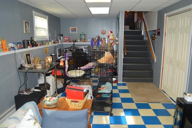basement featuring tile patterned floors, stairway, baseboard heating, and a drop ceiling
