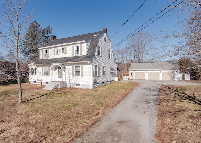 colonial inspired home with an outdoor structure, a front yard, roof with shingles, a chimney, and a detached garage