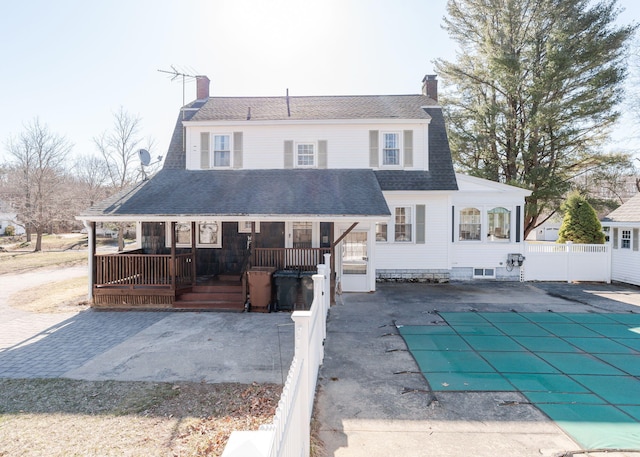 view of front of home with fence, covered porch, roof with shingles, a chimney, and a fenced in pool