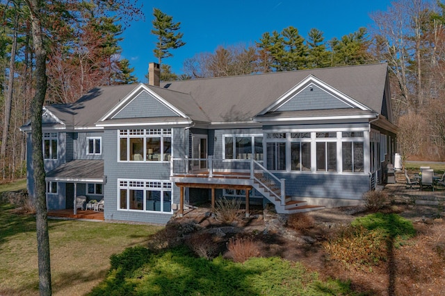 back of property featuring a patio, a chimney, a deck, a lawn, and a sunroom
