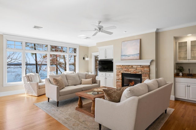 living area with ornamental molding, a ceiling fan, light wood-style flooring, and a fireplace
