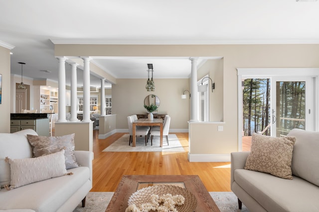 living room featuring crown molding, baseboards, light wood-style flooring, and ornate columns