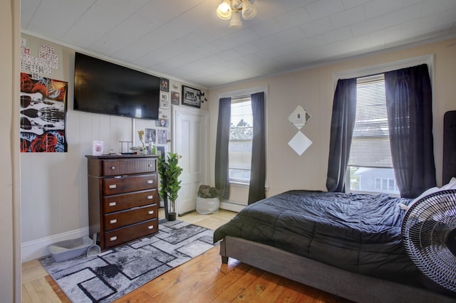 bedroom featuring wood-type flooring, crown molding, and baseboard heating