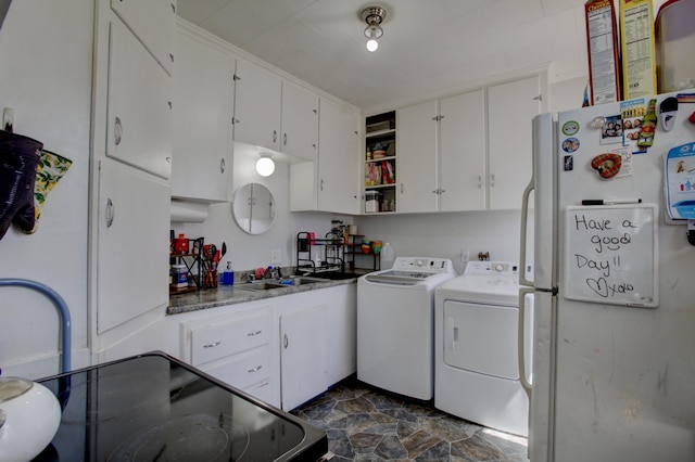 clothes washing area with separate washer and dryer, a sink, and stone finish flooring