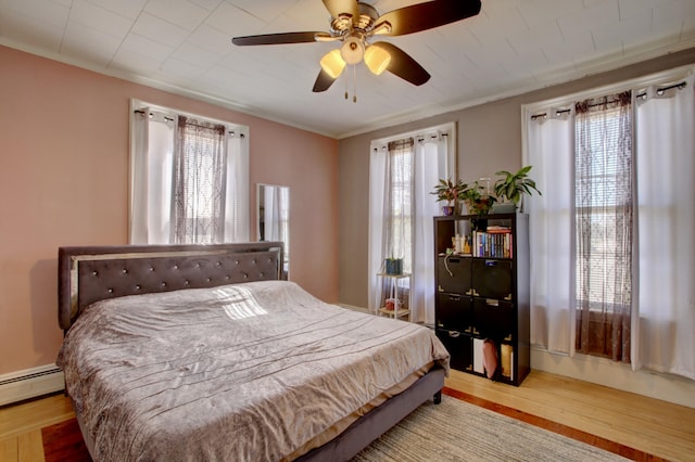 bedroom featuring ornamental molding, a baseboard heating unit, a ceiling fan, and wood finished floors