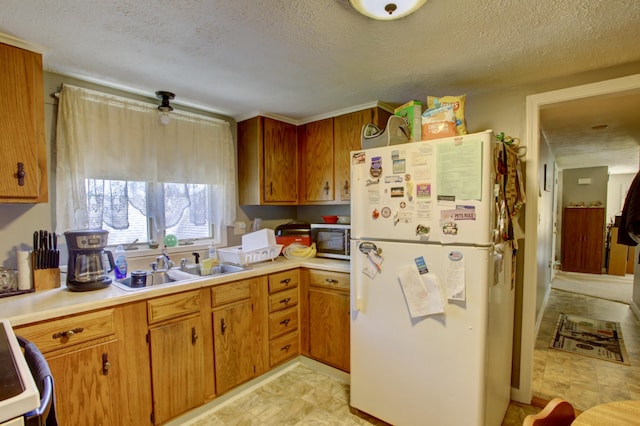 kitchen with light countertops, freestanding refrigerator, stainless steel microwave, and a sink