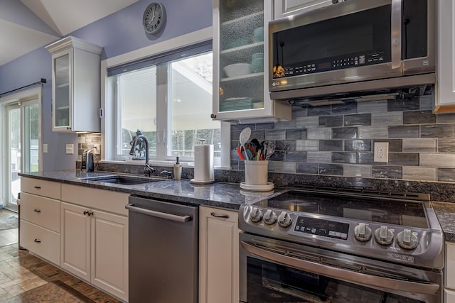 kitchen featuring decorative backsplash, white cabinets, glass insert cabinets, a sink, and appliances with stainless steel finishes
