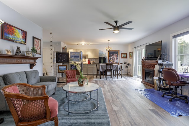 living area with a glass covered fireplace, ceiling fan, and light wood finished floors