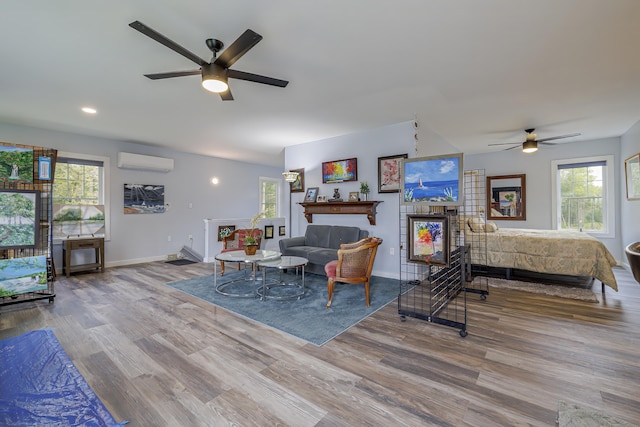 living area with a wall mounted air conditioner, wood finished floors, ceiling fan, and plenty of natural light