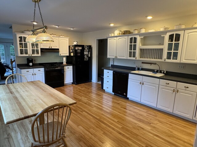 kitchen with under cabinet range hood, white cabinets, black appliances, dark countertops, and a sink