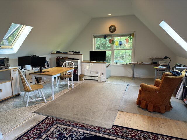 additional living space with wood finished floors, vaulted ceiling with skylight, a toaster, baseboard heating, and baseboards