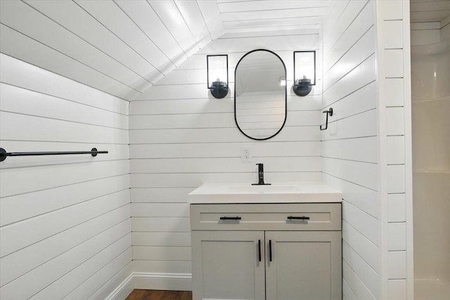 bathroom with vanity, wood walls, lofted ceiling, and wood finished floors