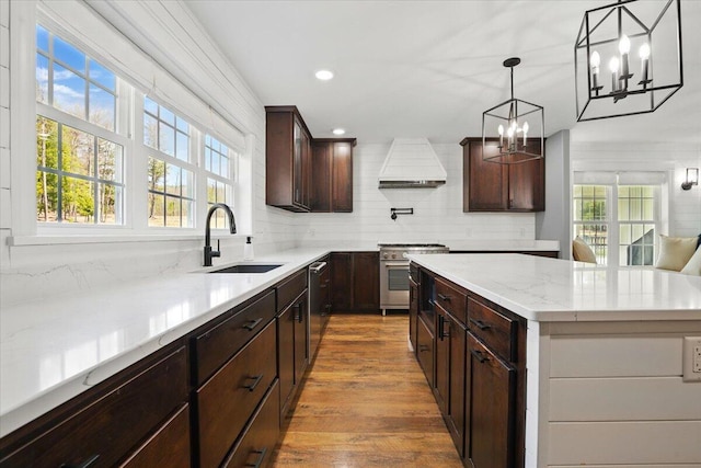 kitchen with an inviting chandelier, wood finished floors, custom range hood, a sink, and stainless steel appliances