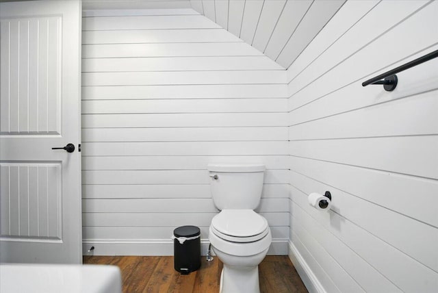 bathroom featuring baseboards, wood finished floors, wooden walls, and toilet