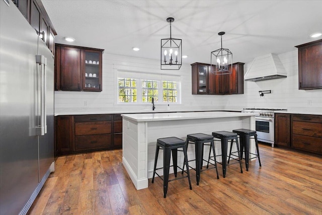 kitchen featuring high quality appliances, an inviting chandelier, a kitchen breakfast bar, premium range hood, and glass insert cabinets