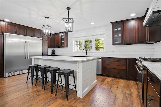 kitchen featuring a breakfast bar area, dark wood-style flooring, high quality appliances, a center island, and under cabinet range hood