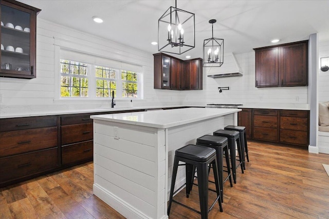 kitchen with an inviting chandelier, dark wood-style flooring, dark brown cabinetry, a kitchen breakfast bar, and a sink