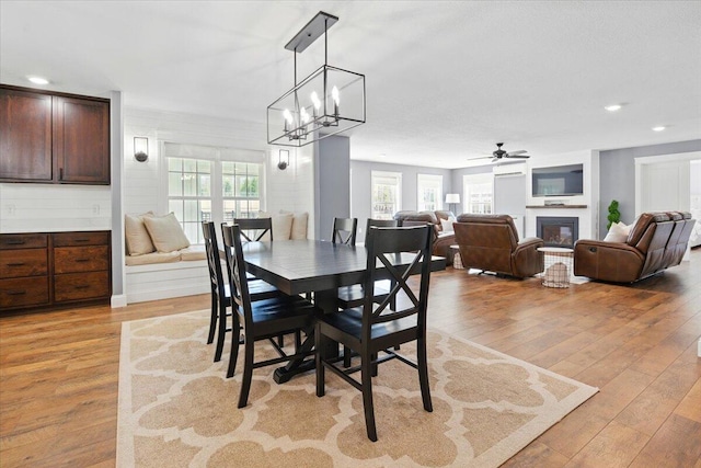 dining area with a glass covered fireplace, ceiling fan with notable chandelier, recessed lighting, and light wood-style flooring