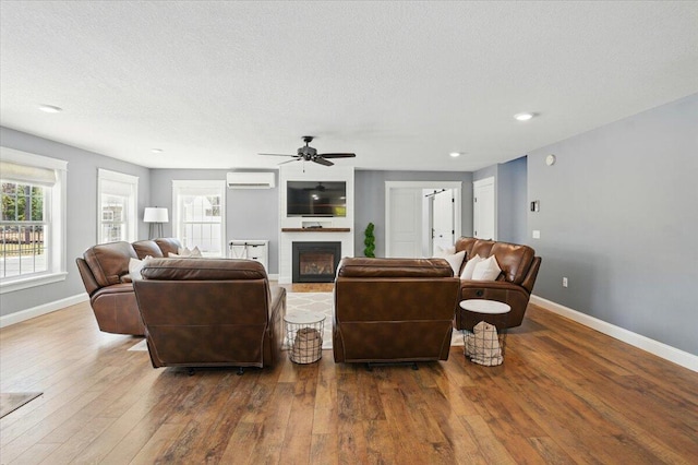 living area featuring a fireplace, hardwood / wood-style floors, a ceiling fan, baseboards, and a wall unit AC