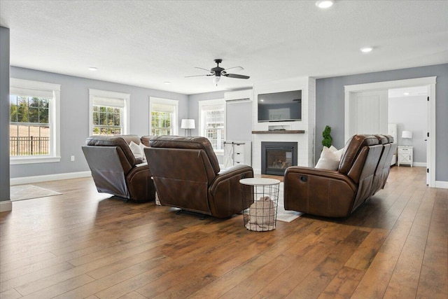 living area with a glass covered fireplace, baseboards, a ceiling fan, and dark wood finished floors
