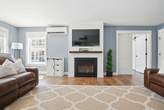living room with an AC wall unit, baseboards, wood finished floors, and a large fireplace